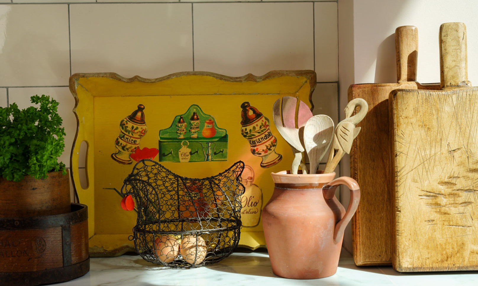 Vintage kitchen shelf styling with antique wooden chopping boards, yellow serving tray, pink ceramic jug and collected home decor.