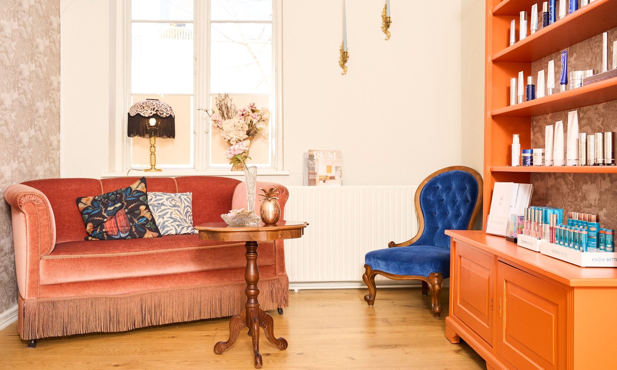 Colourful vintage-inspired sitting room with coral velvet sofa, blue armchair, and orange bookshelves creating a collected, eclectic interior