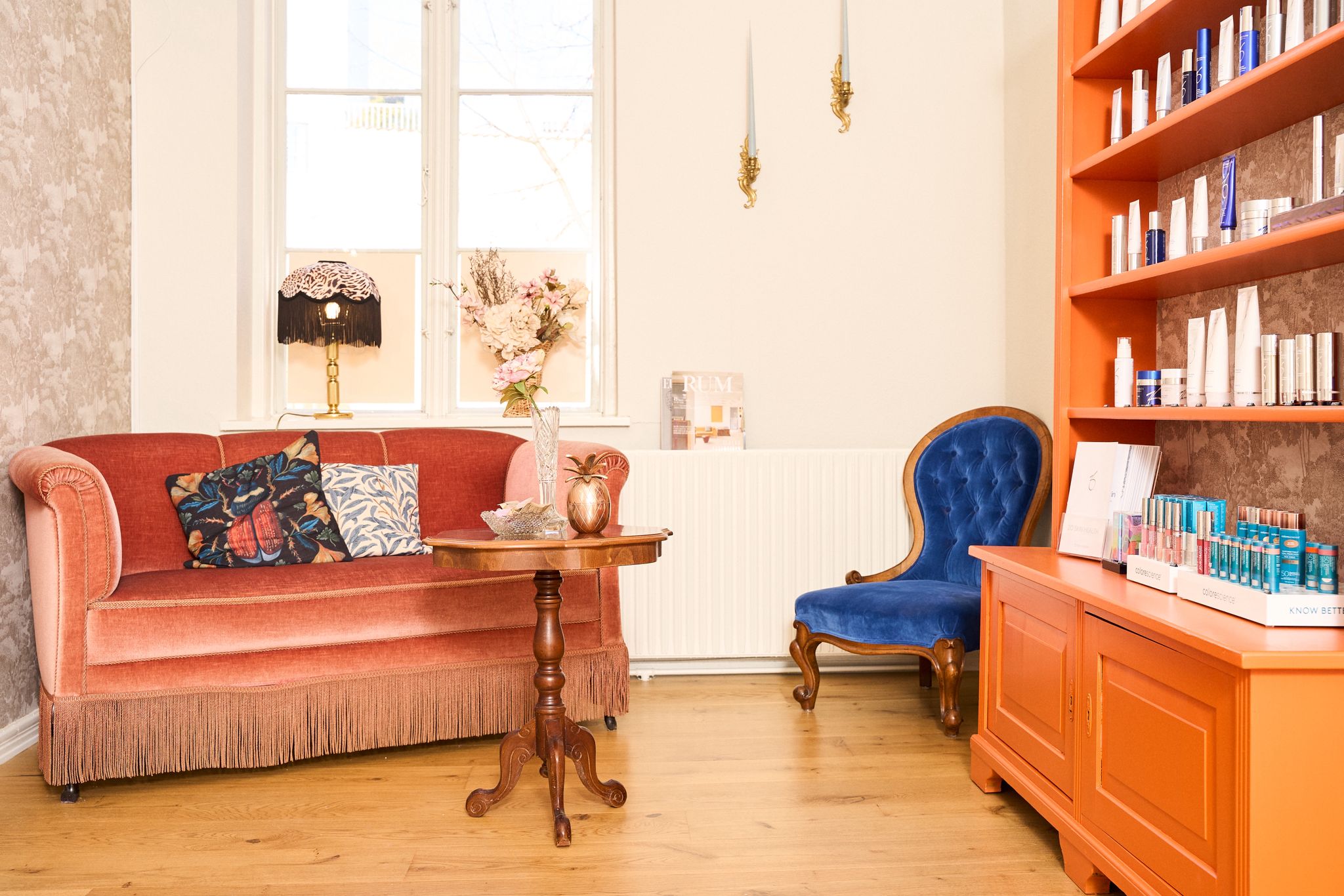 Colourful vintage-inspired sitting room with coral velvet sofa, blue armchair, and orange bookshelves creating a collected, eclectic interior